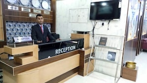 A reception desk with a sign labeled "RECEPTION," a wall clock, and a flat-screen TV mounted above it. - Hotel Embassy International (Muzaffarpur)