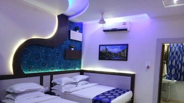 A hotel room with two beds, a wall-mounted air conditioner, a picture of a cityscape, and a bathroom with a sink and mirror. - Hotel Embassy International (Muzaffarpur)