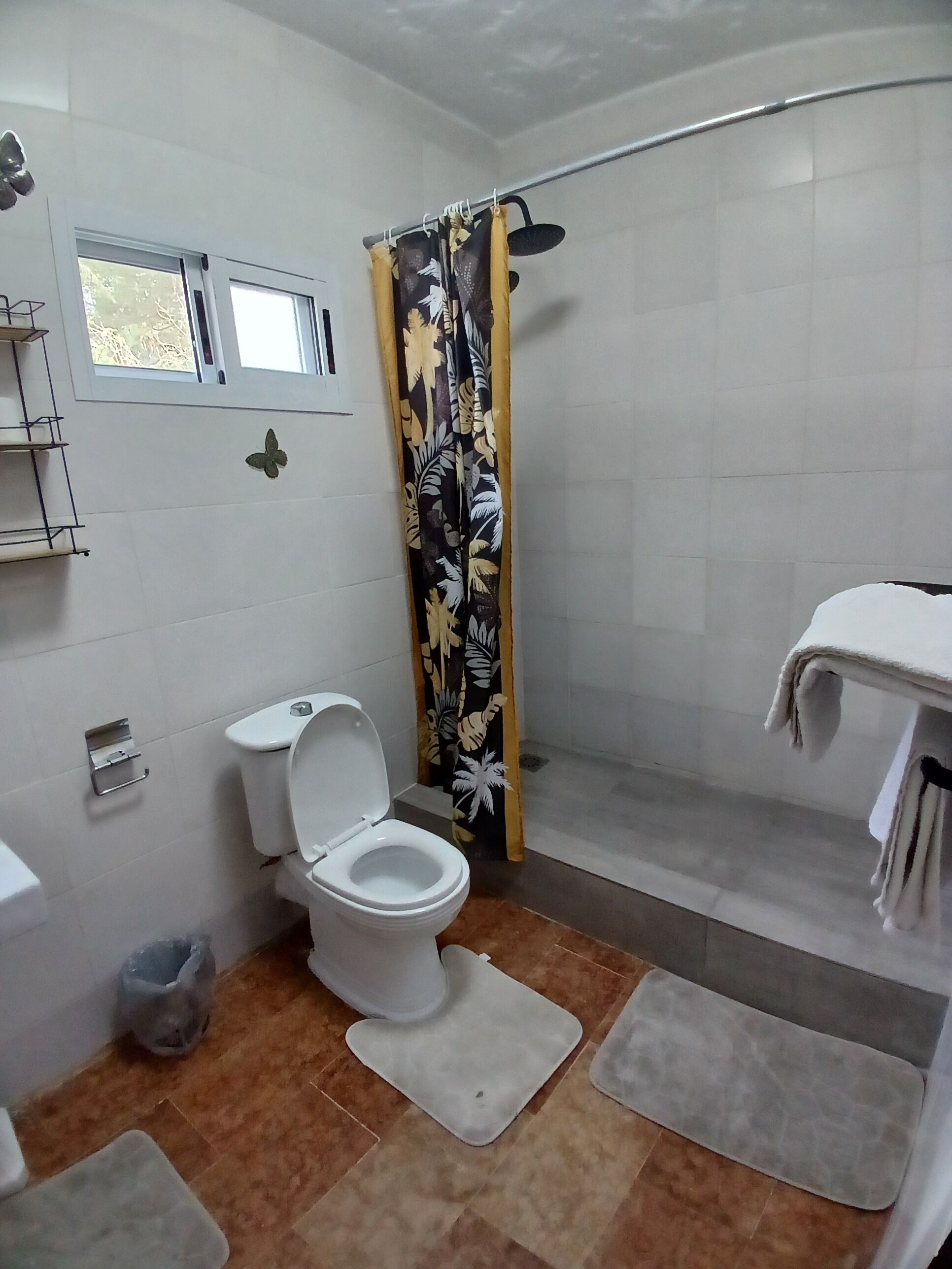 A bathroom with a toilet, shower, and a window.