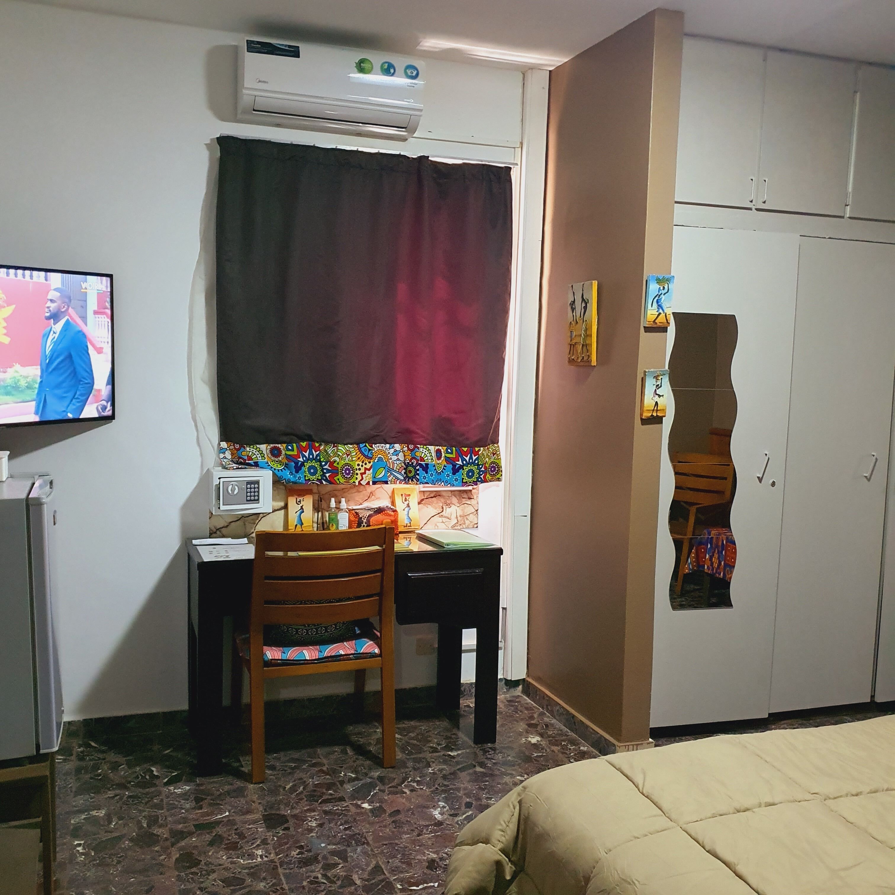 Un dormitorio con una cama, un escritorio con silla, aire acondicionado, televisor y armario.