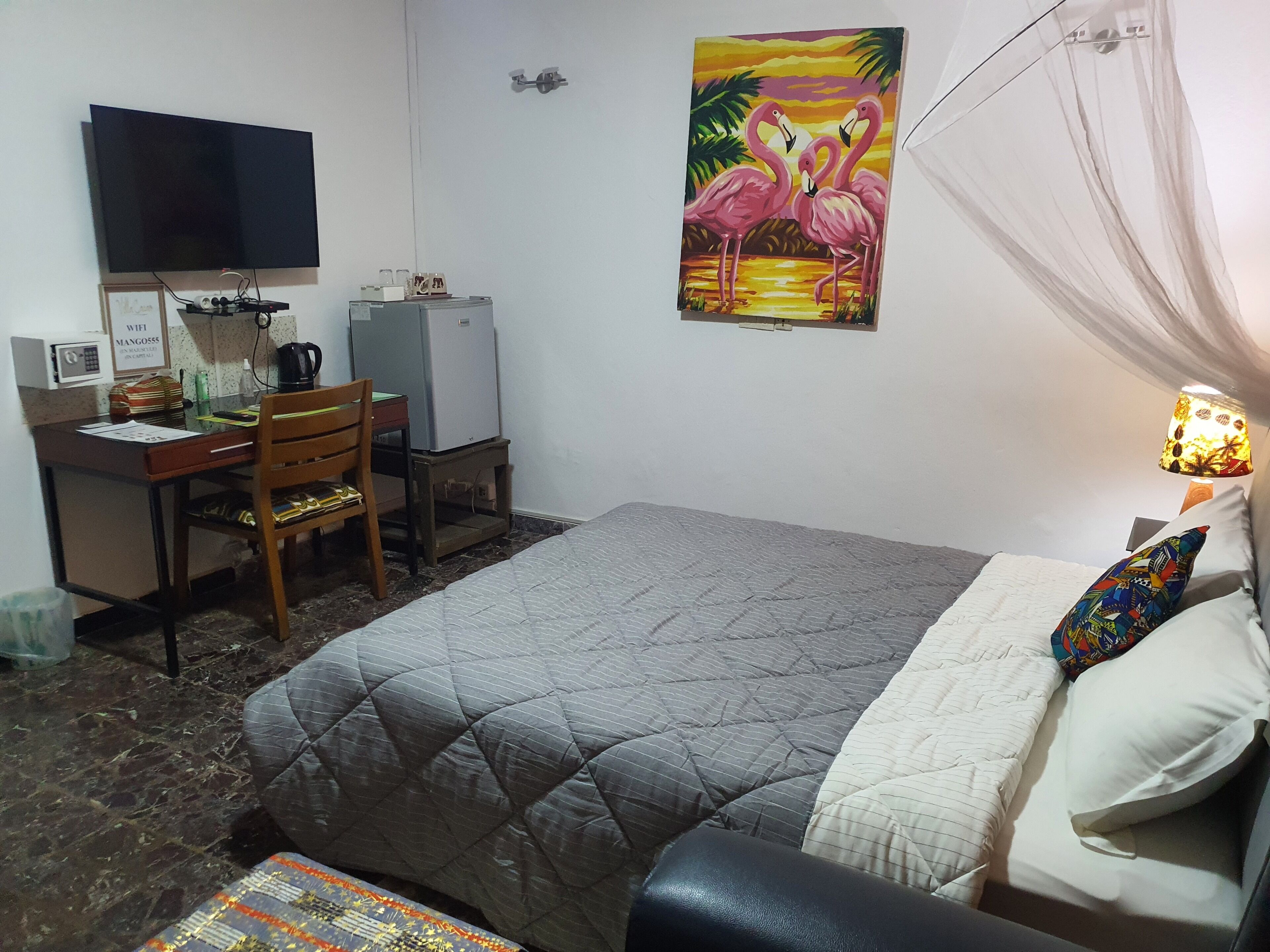 A hotel room with a bed, a desk with a computer, a chair, a TV, and a painting on the wall.