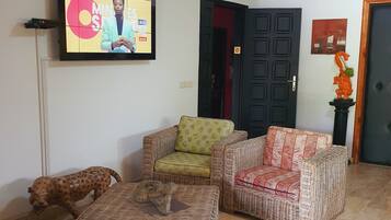 A living room with wicker furniture, a television mounted on the wall, and a door with a decorative handle.