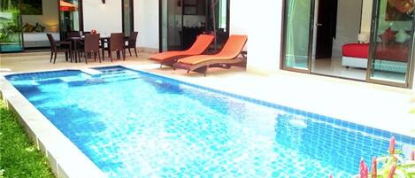 A swimming pool with lounge chairs and umbrellas, surrounded by a well-maintained lawn and a glass door leading to a room.