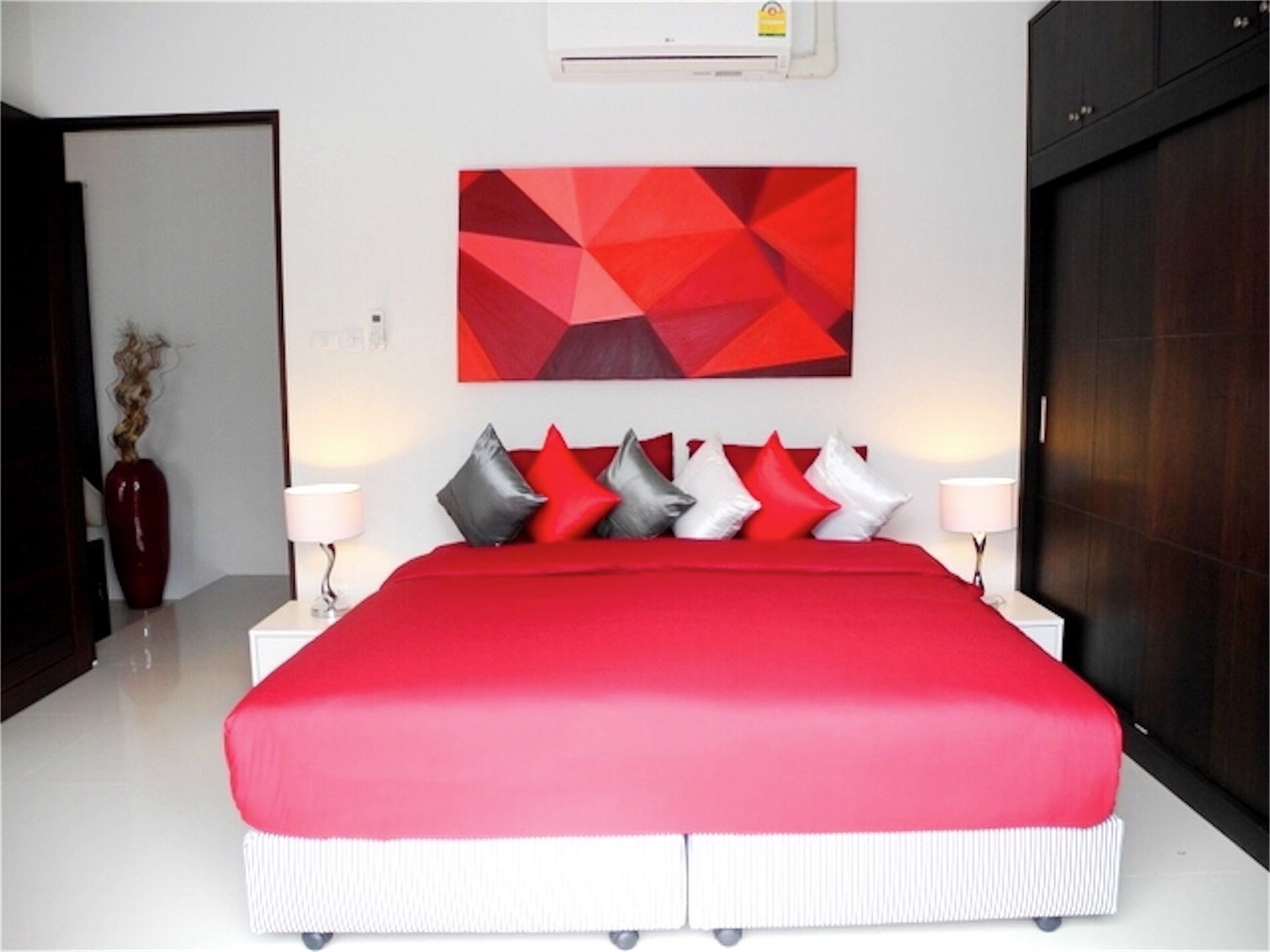 Un dormitorio moderno con una cama grande, una obra de arte geométrica roja en la pared y un armario de madera oscura.