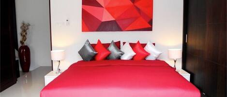 Un dormitorio moderno con una cama grande, una obra de arte geométrica roja en la pared y un armario de madera oscura.
