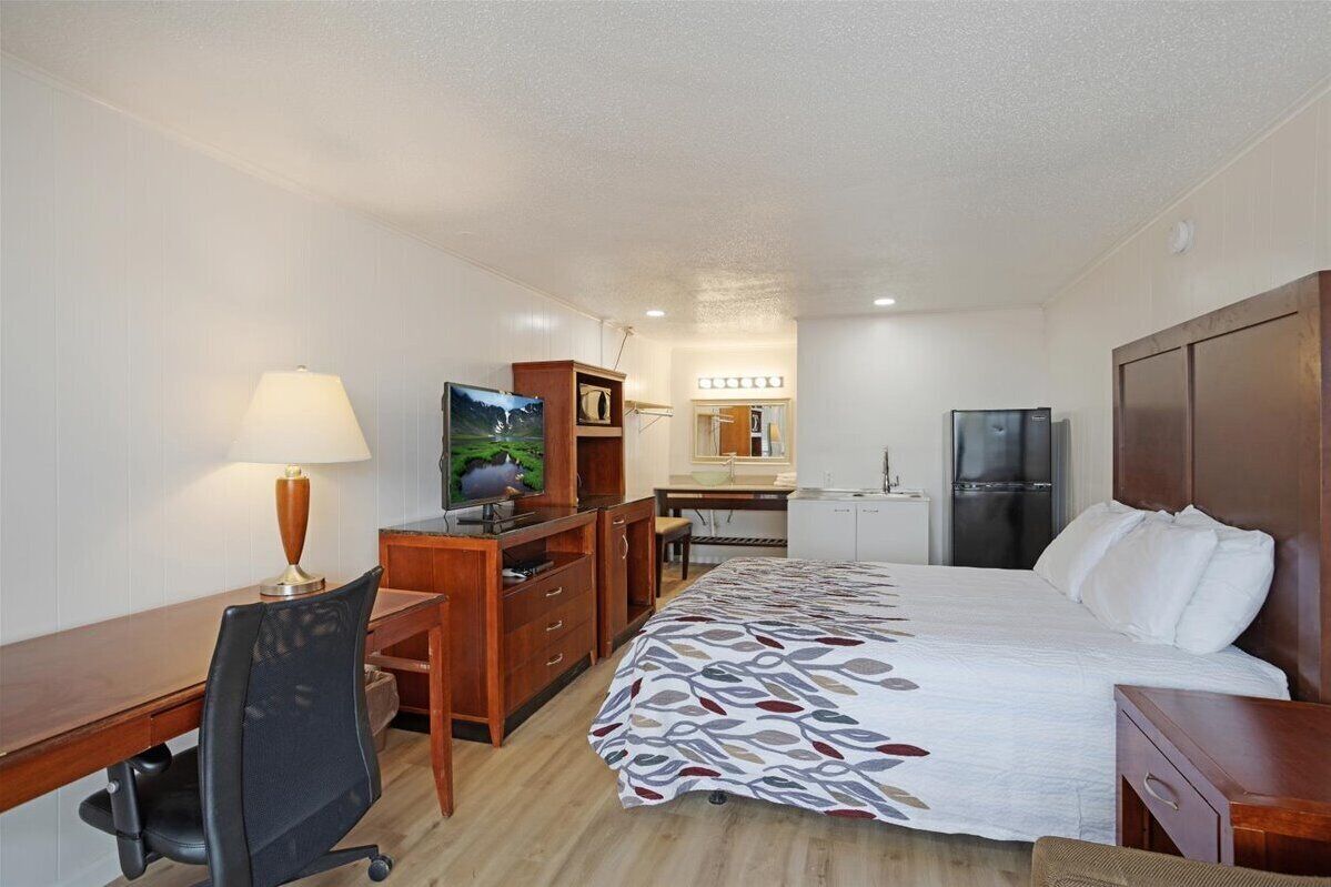 Een hotelkamer met een bed, bureau, stoel, televisie en kitchenette.