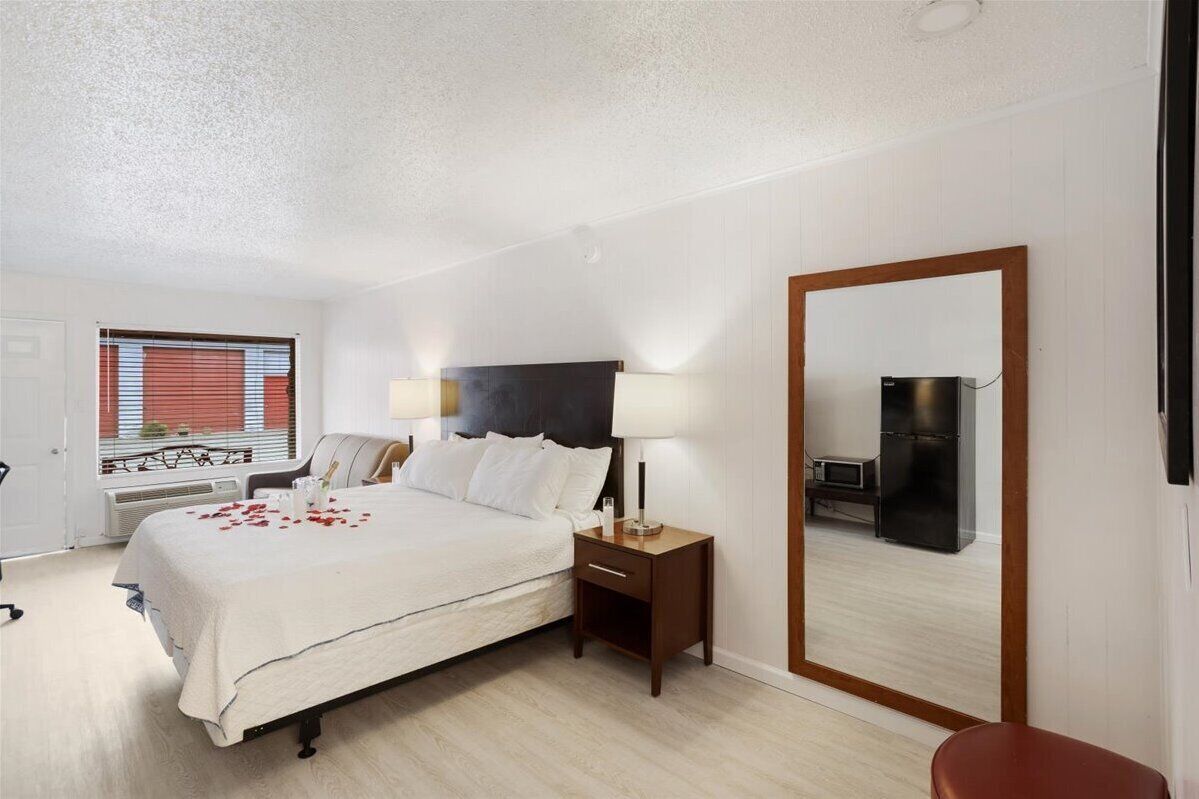 A bedroom with a bed, bedside tables, a mirror, and a window with blinds.