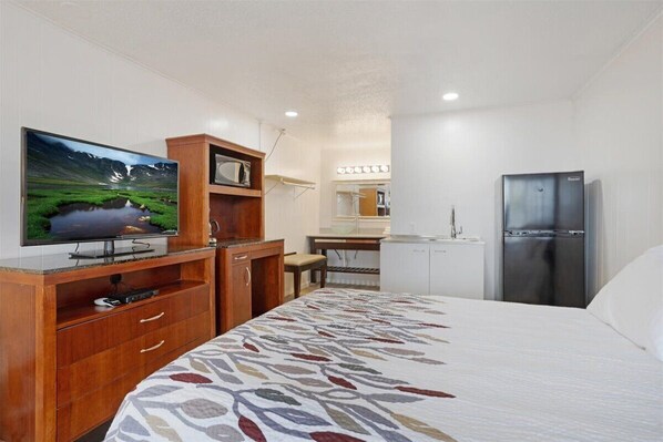Habitación de hotel con cama, televisor, mueble de madera, refrigerador y pequeña kitchenette.