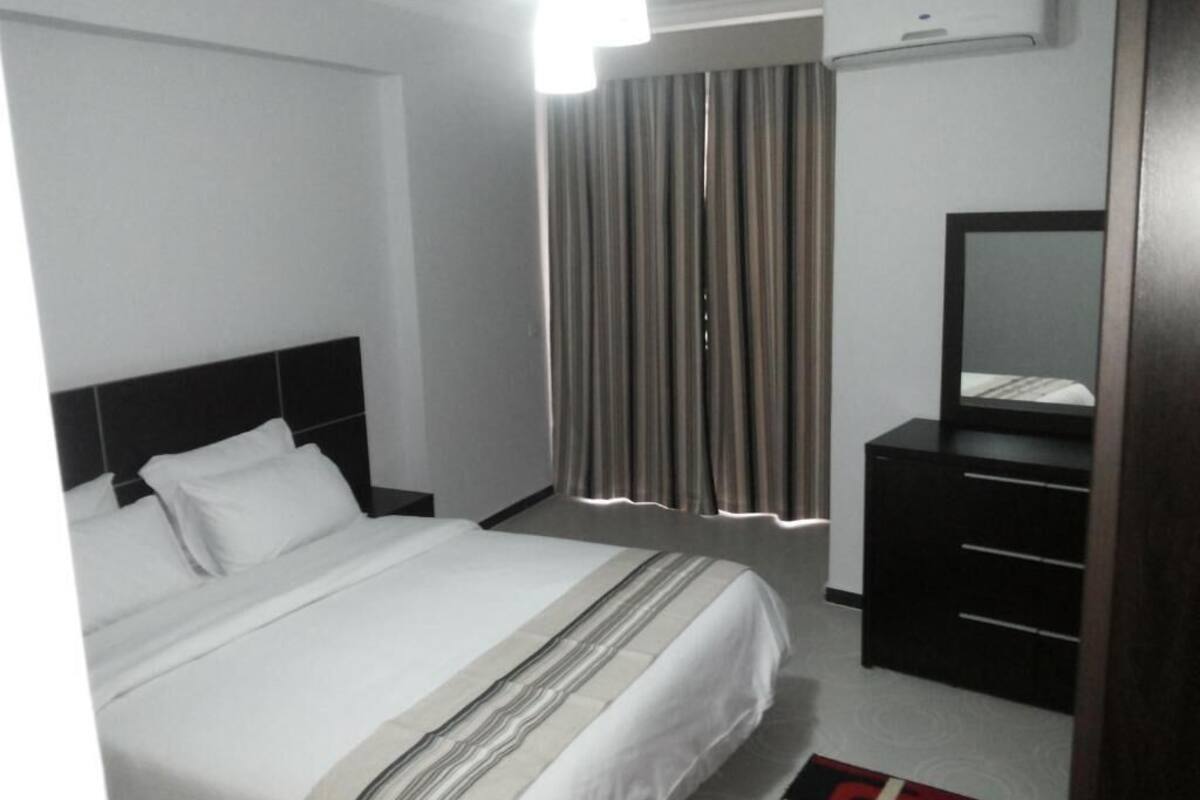 A hotel room with a bed, a nightstand, a dresser, a mirror, and a window with curtains.