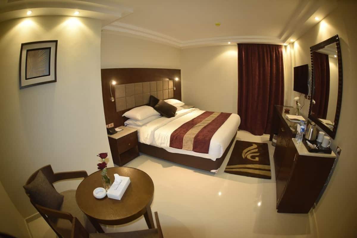 A hotel room with a bed, bedside table, chair, and a desk with a mirror.