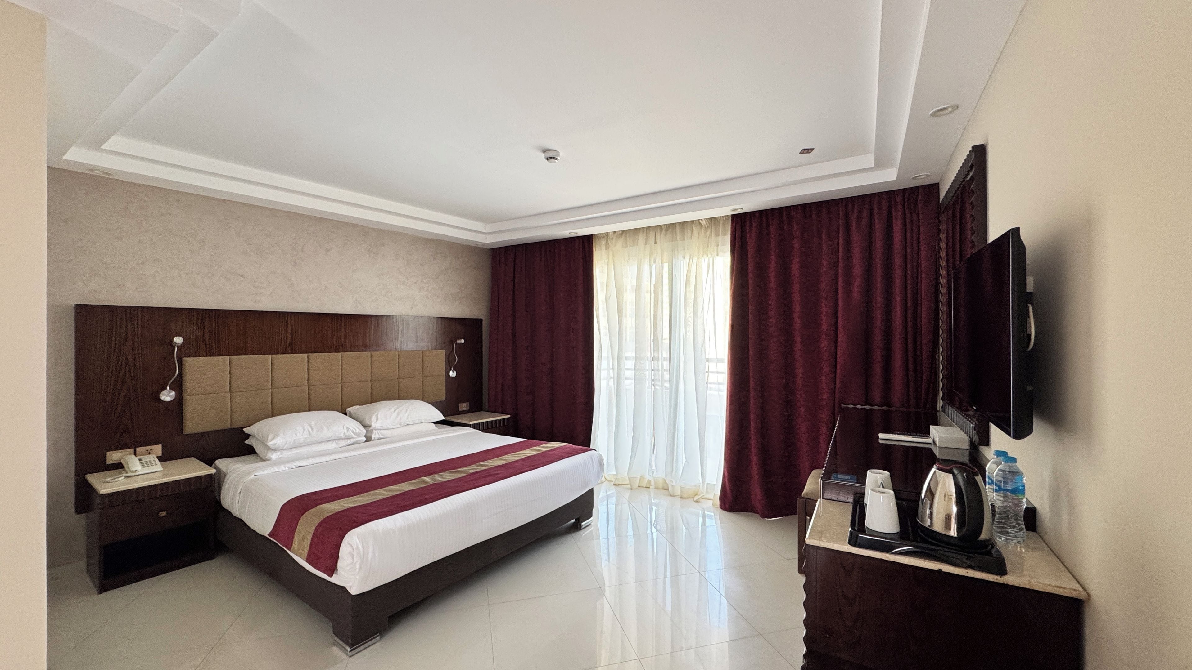 A hotel room with a large bed, a bedside table with a phone, a flat-screen TV mounted on the wall, and a mirror.