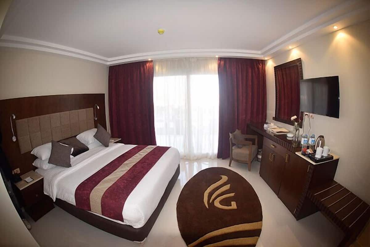A hotel room with a large bed, a desk, a chair, a TV, and a bathroom.