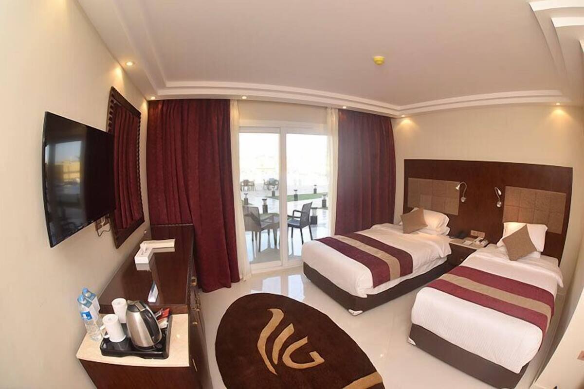 A hotel room with two beds, a TV, a desk with a coffee maker, and a view of the outdoors.