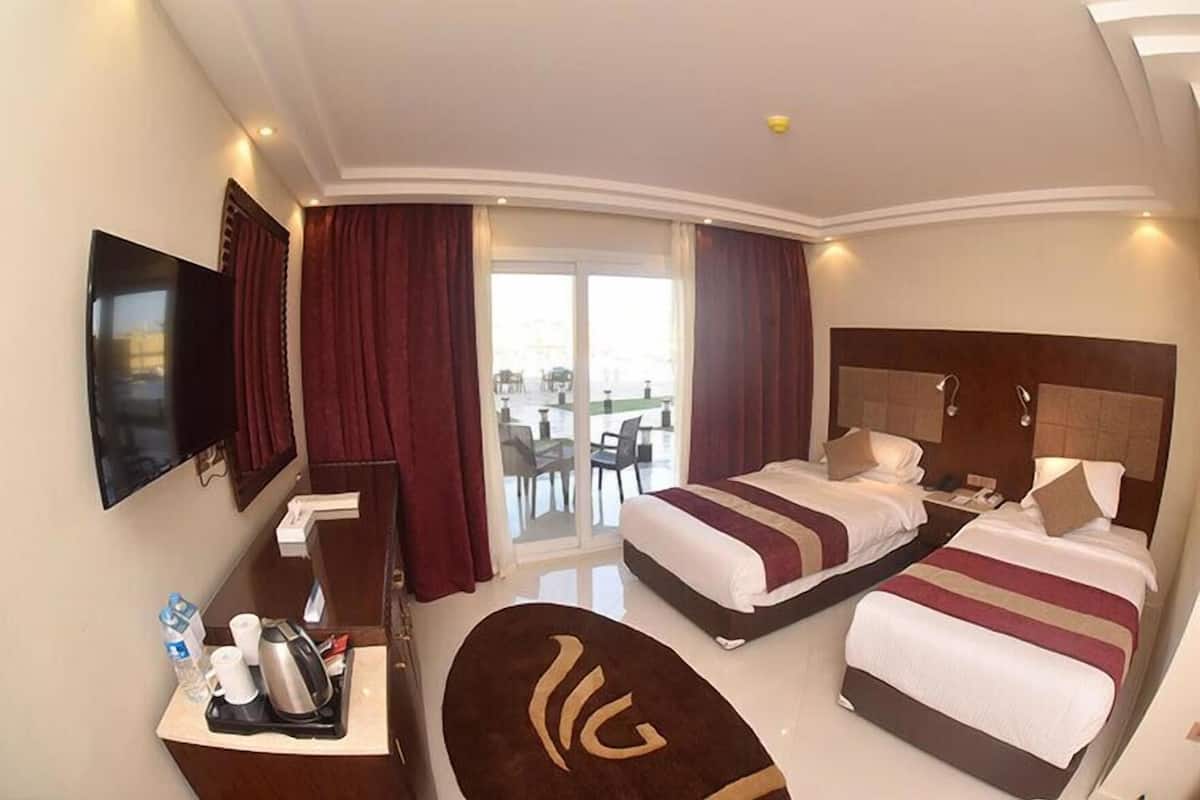 A hotel room with two beds, a desk with a flat-screen TV, a coffee maker, and a view of the outdoors.