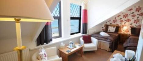 Un salón acogedor con sofá, sillón y mesa de centro. Se ve una ventana con vistas, una araña y una lámpara.