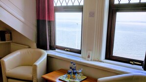 A room with two white leather armchairs, a wooden table with a tray of bottled water and juice, and a view of the sea through two windows with metal grilles. - The Craigwell Hotel (Morecambe)