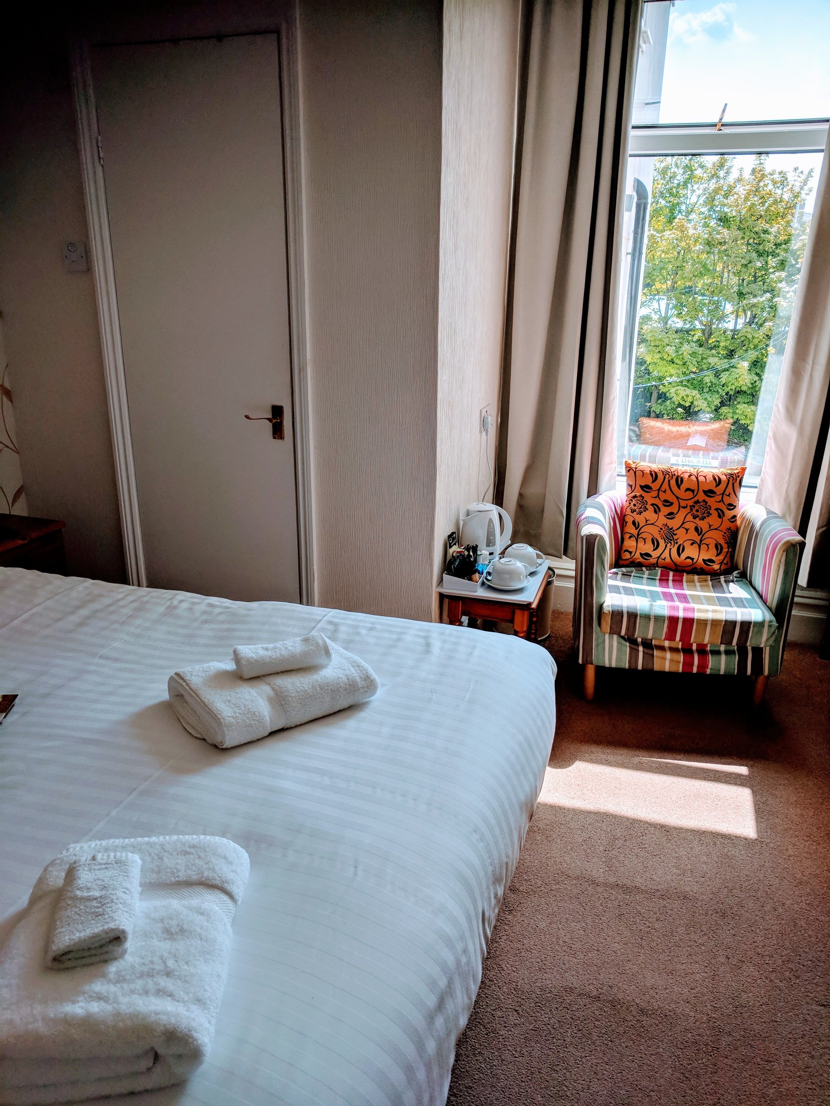 Una habitación de hotel con cama, una silla y ventana con vistas a árboles.