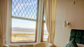 A hotel room with a large window, a bed with green and white bedding, a green upholstered headboard, and a small table with a lamp. - The Craigwell Hotel (Morecambe)