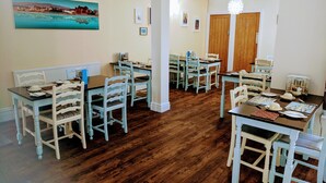 A dining area with multiple tables and chairs, wooden floors, and a painting on the wall. - The Craigwell Hotel (Morecambe)