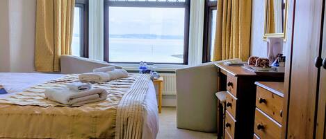 Una habitación de hotel con cama, escritorio, silla, cómoda y un ventanal con cortinas.
