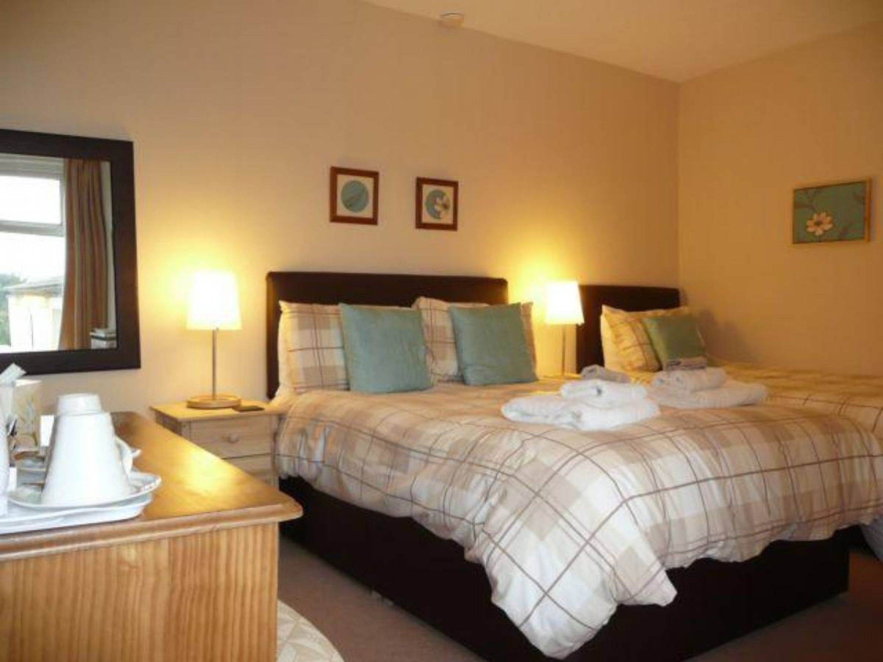 A hotel room with a bed, two bedside lamps, a wooden dresser, and a mirror.