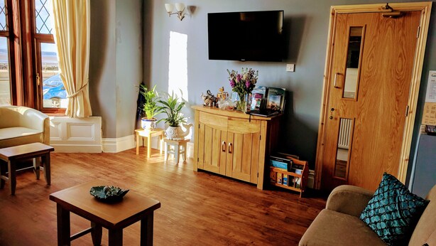 A living room with a wooden floor, a sofa, a table, a TV mounted on the wall, and a door with a mirror. - The Craigwell Hotel (Morecambe)