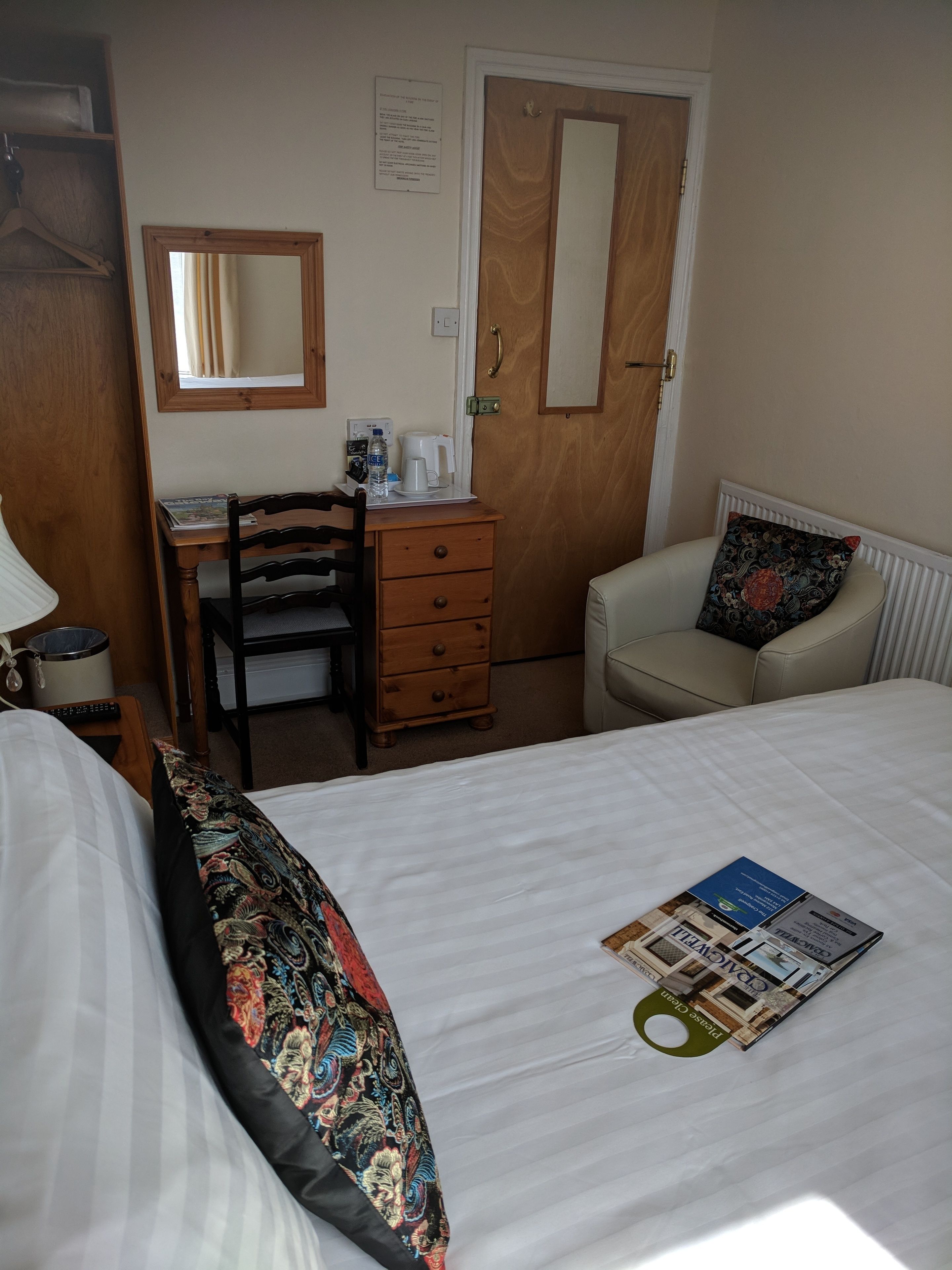 A hotel room with a bed, a desk with a chair, a dresser, a door, and a window.