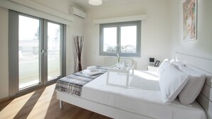 A modern bedroom with a large bed, a bedside table, a window, and a view of the city.