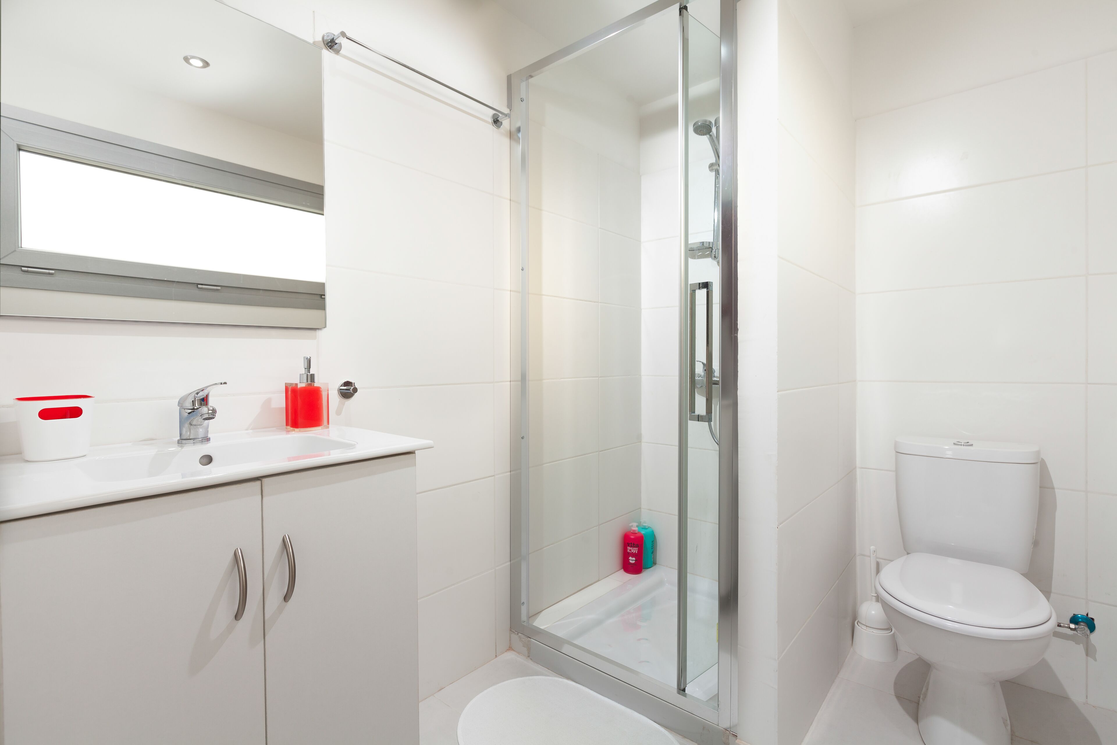 A modern bathroom with a glass-enclosed shower, a white sink with a mirror above it, and a toilet.