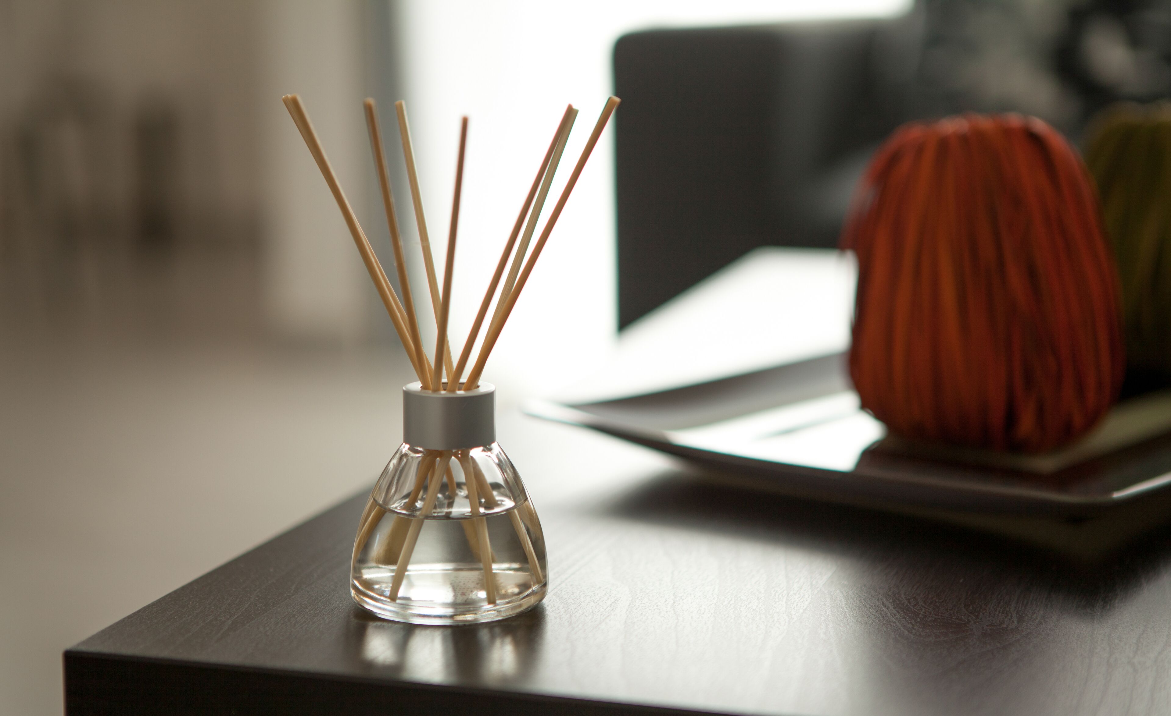 A clear glass bottle with reed sticks, placed on a wooden table.