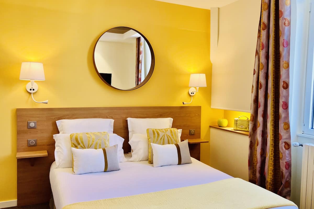 A hotel room with a large bed, two bedside tables, a round mirror, and two wall-mounted lamps.