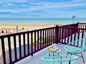 A balcony with a view of the beach, featuring wicker chairs and a small table with a tray.