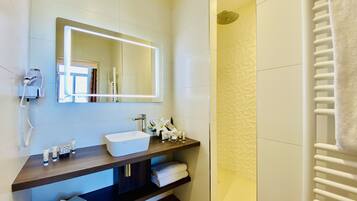 A modern bathroom with a white sink, a large mirror, a towel rack, and a shower area.