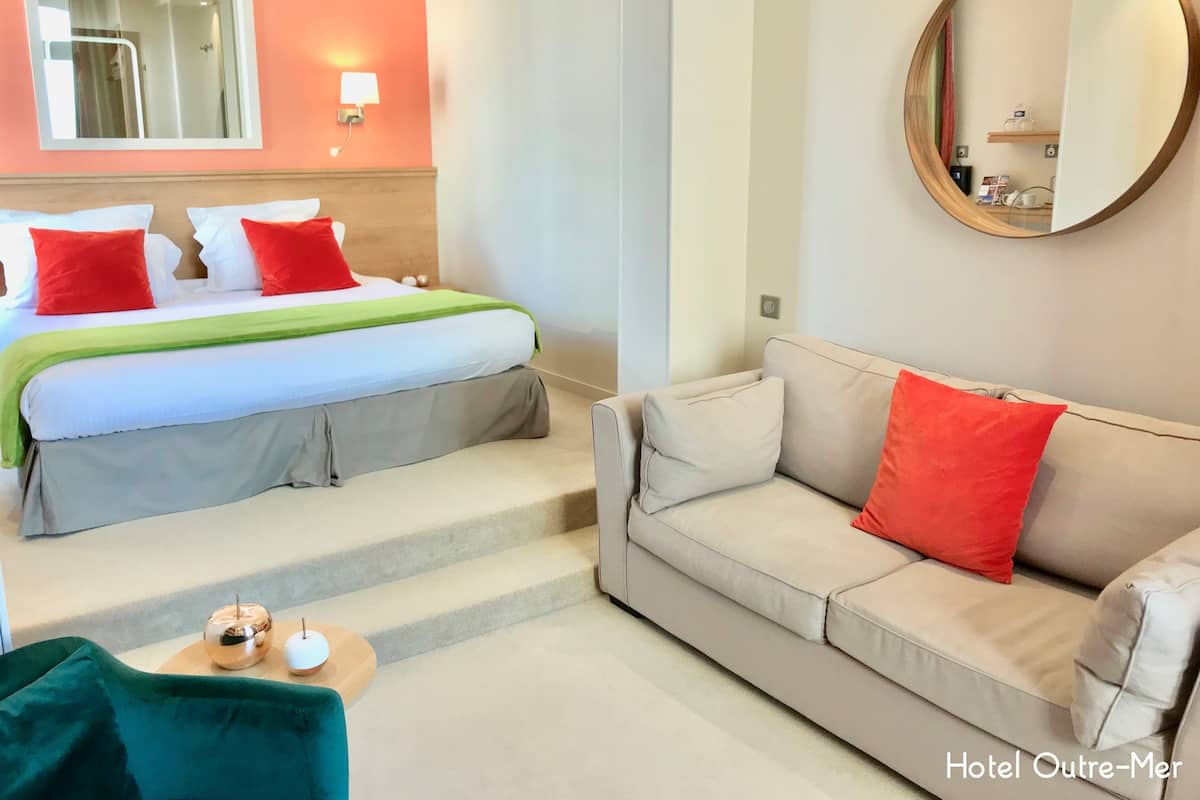 A hotel room with a bed, a sofa, a mirror, and a small table with a candle and a book.