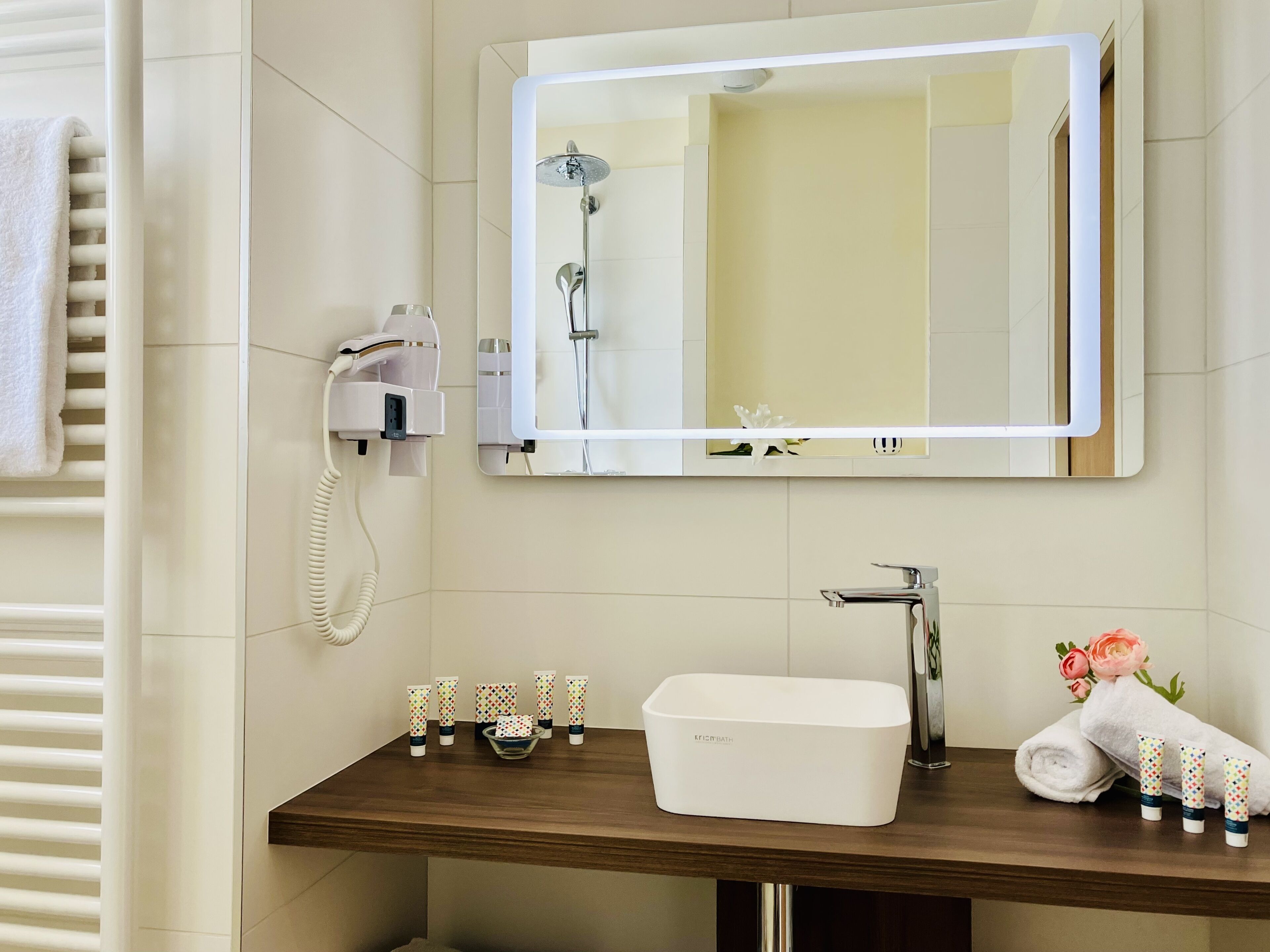 Ein Badezimmer mit Spiegel, Waschbecken, Fön und Pflegeprodukten.