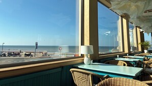 A seaside restaurant with large windows, wicker furniture, and a view of the beach. - Hôtel Outre-Mer (Villers-sur-Mer)
