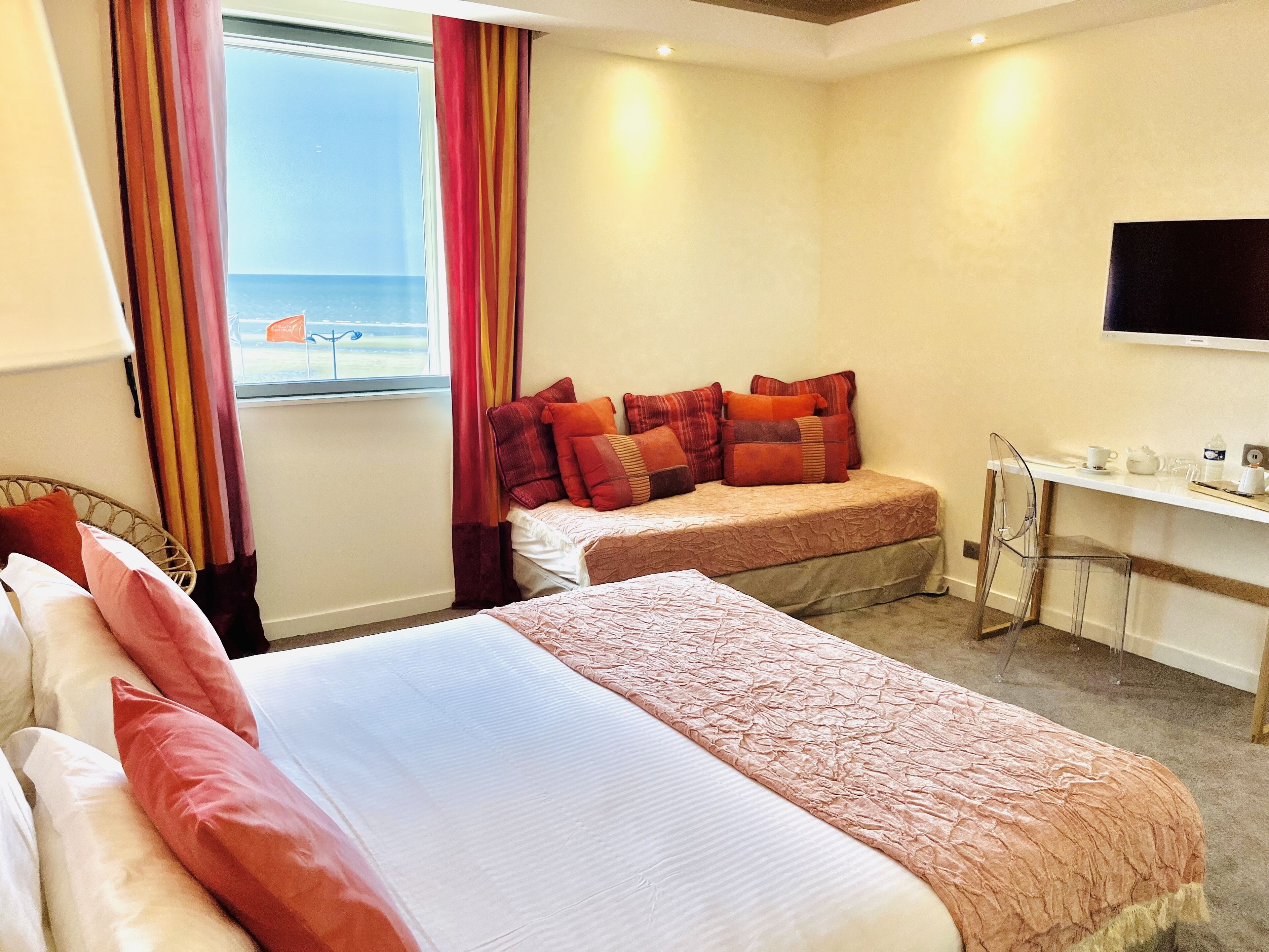 Ein Hotelzimmer mit zwei Betten, einem Schreibtisch, einem Sessel, einem Fernseher und einem Fenster mit Vorhängen.
