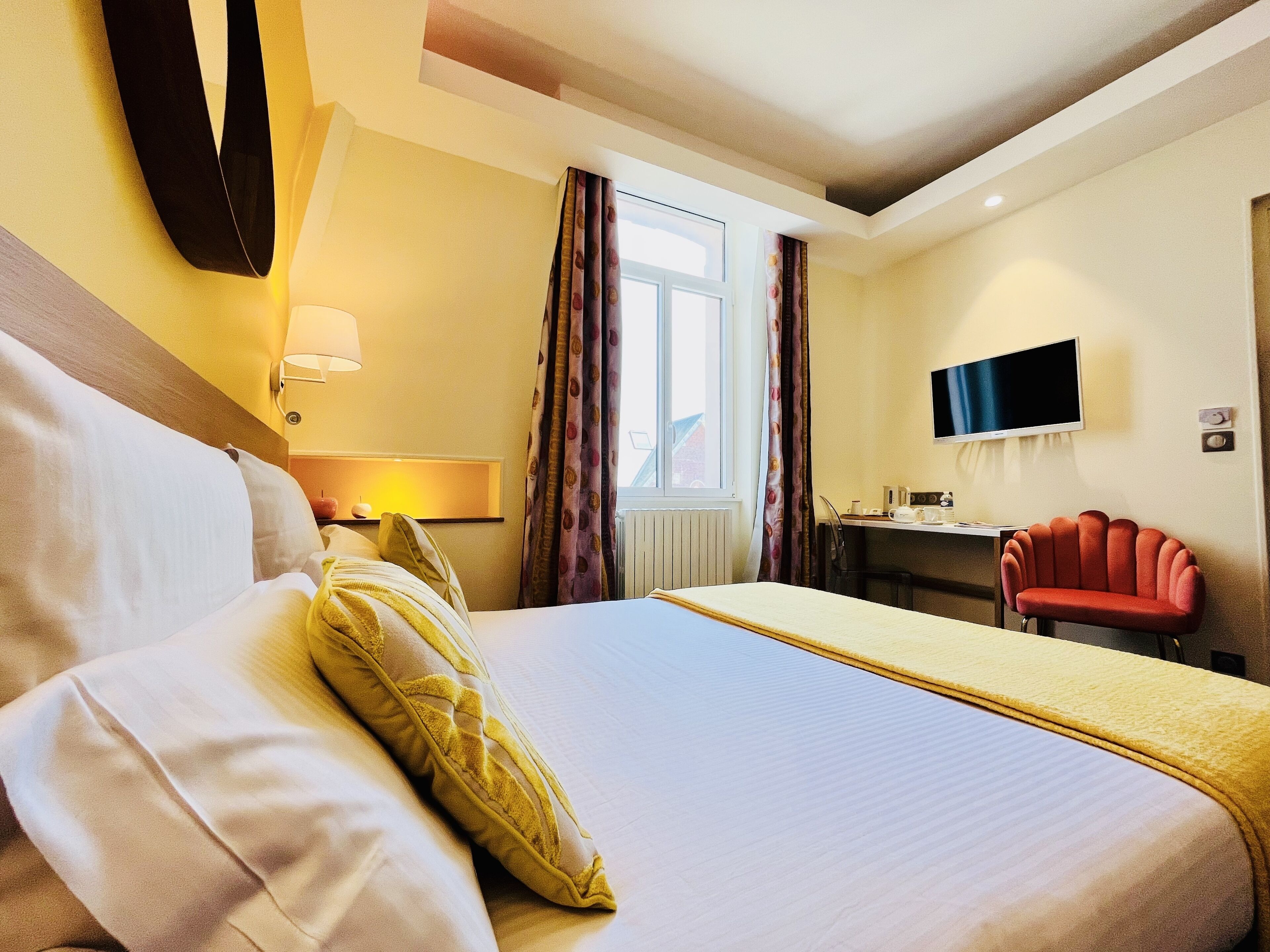 A hotel room with a large bed, a desk with a chair, a television, and a window with curtains.