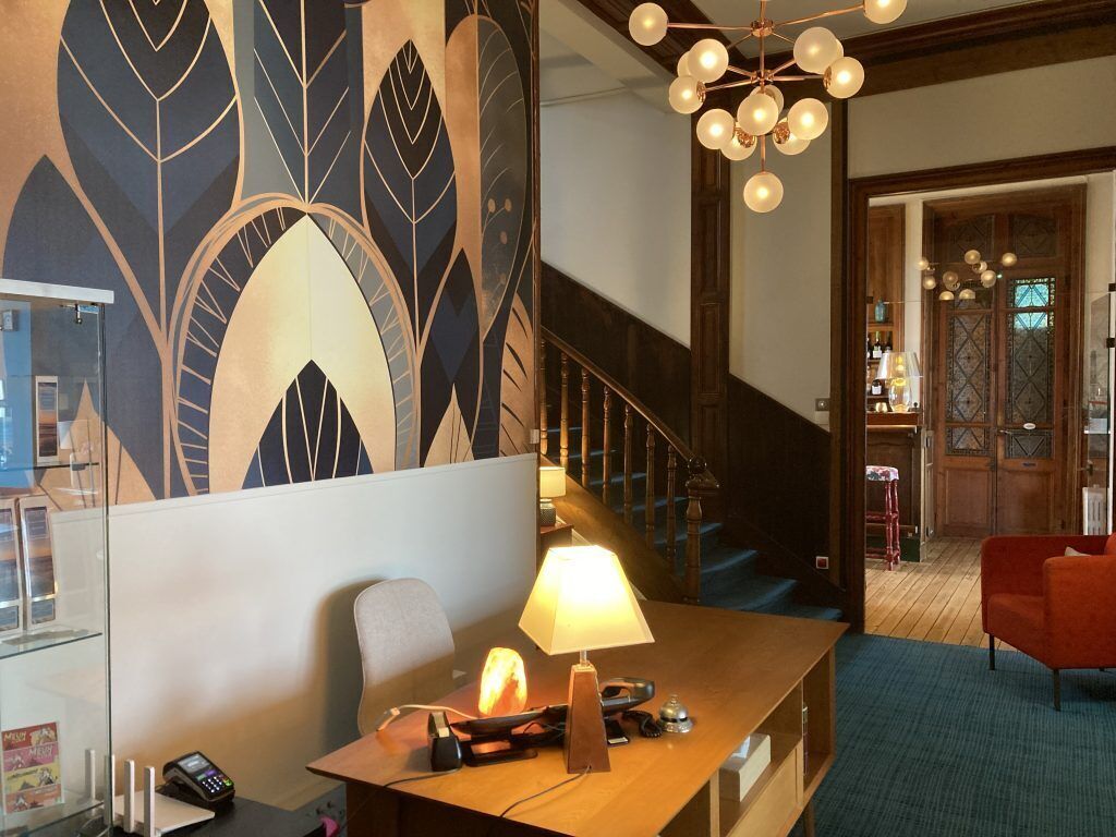 Un vestíbulo de hotel de diseño moderno, con una escalera, un mostrador de recepción con una lámpara y una zona de estar con una silla roja.