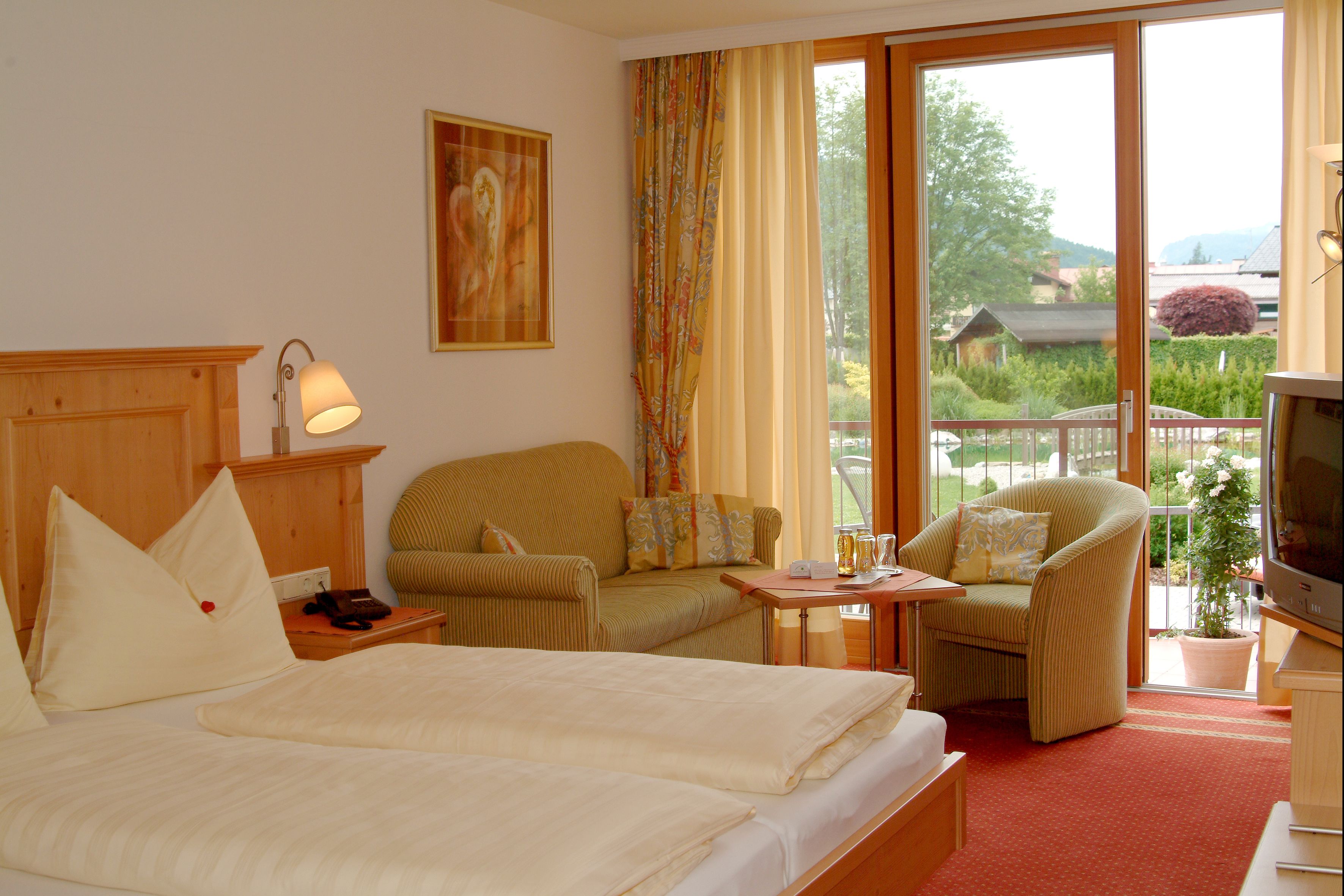 A hotel room with a bed, two chairs, a television, and a window with curtains.