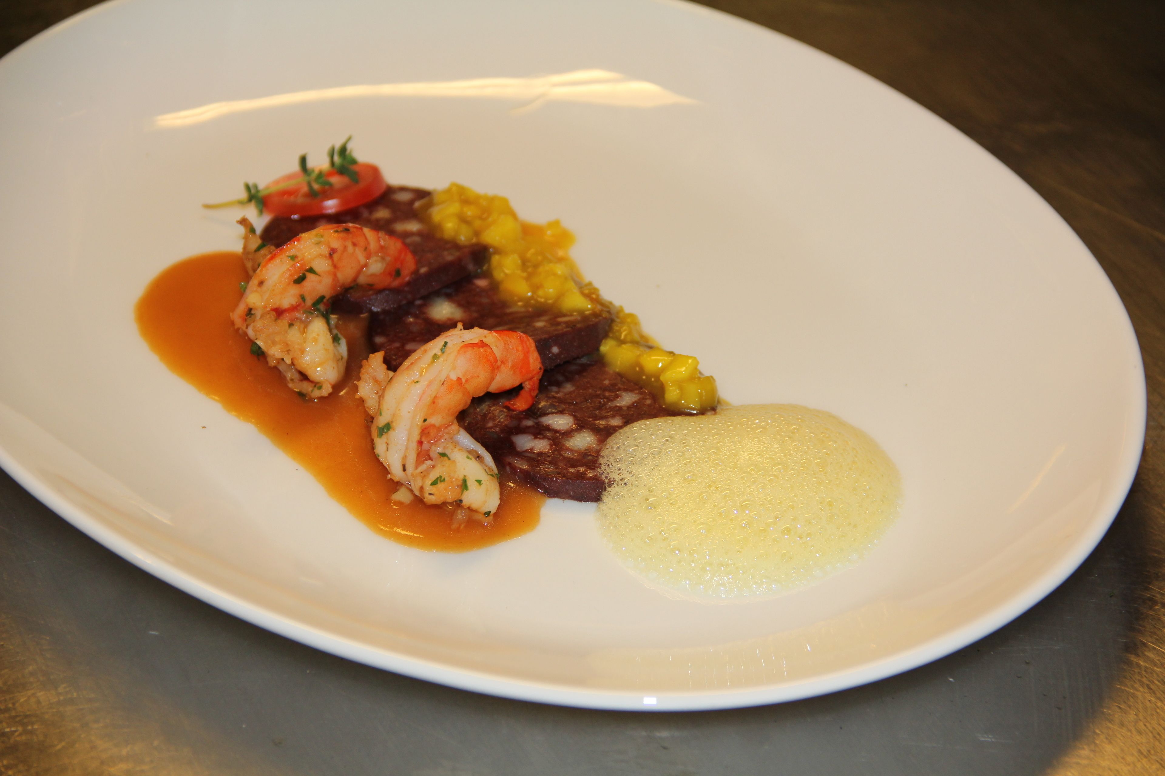 A white plate with a seafood dish, including shrimp and a yellow sauce.