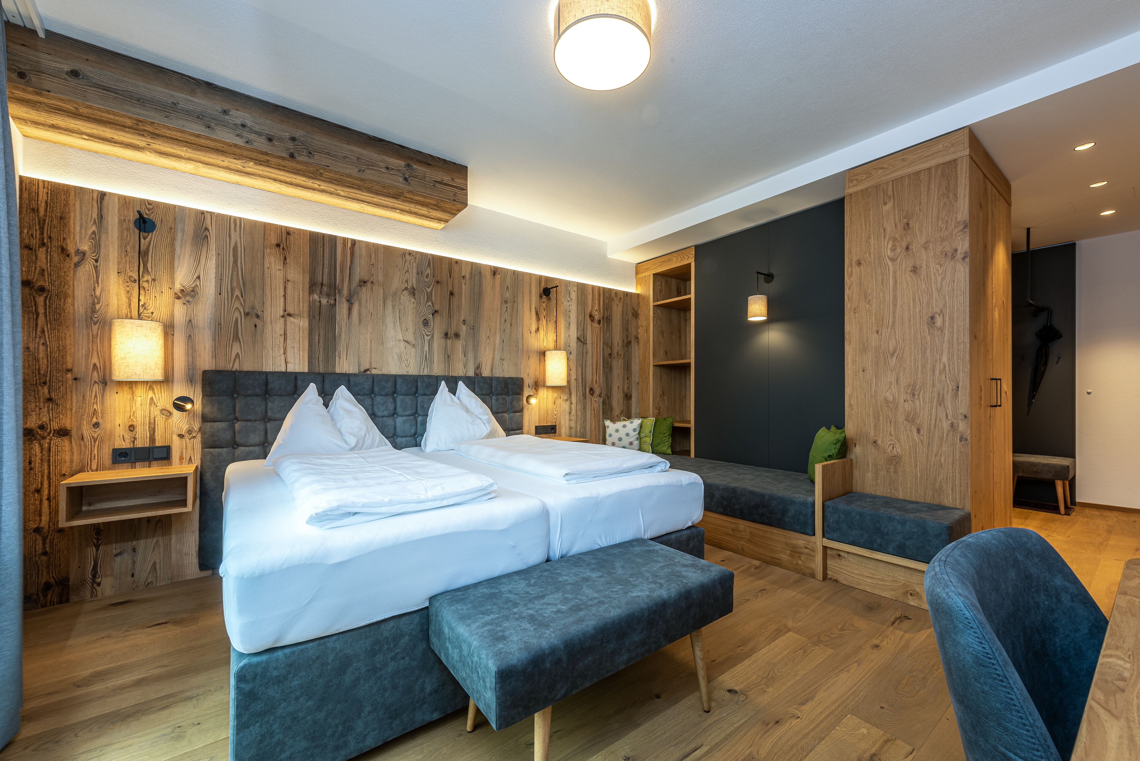 A modern hotel room with a large bed, a bench, and a seating area.