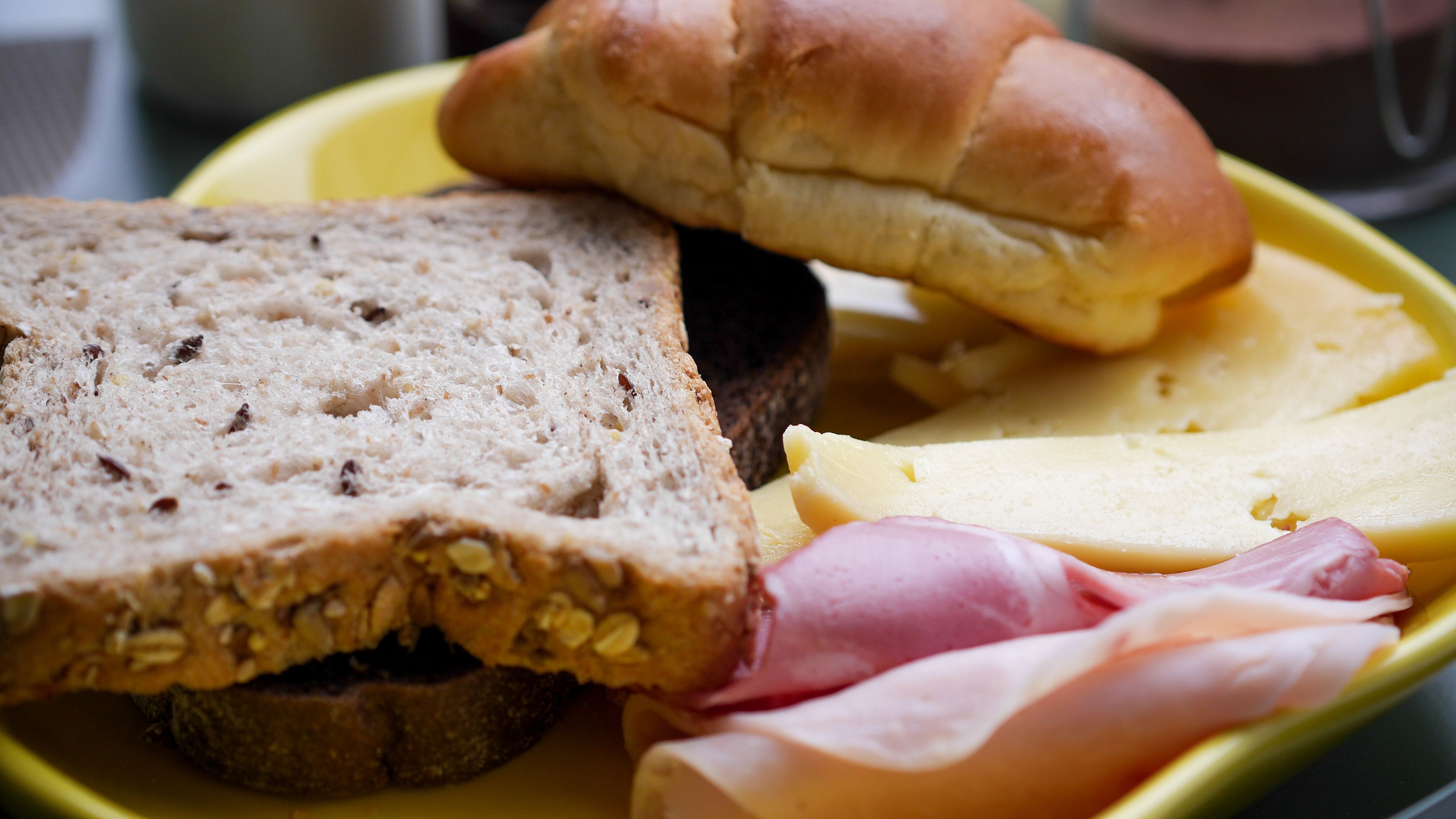 Een bord met plakjes volkorenbrood, een stukje ham, kaas en een broodje.