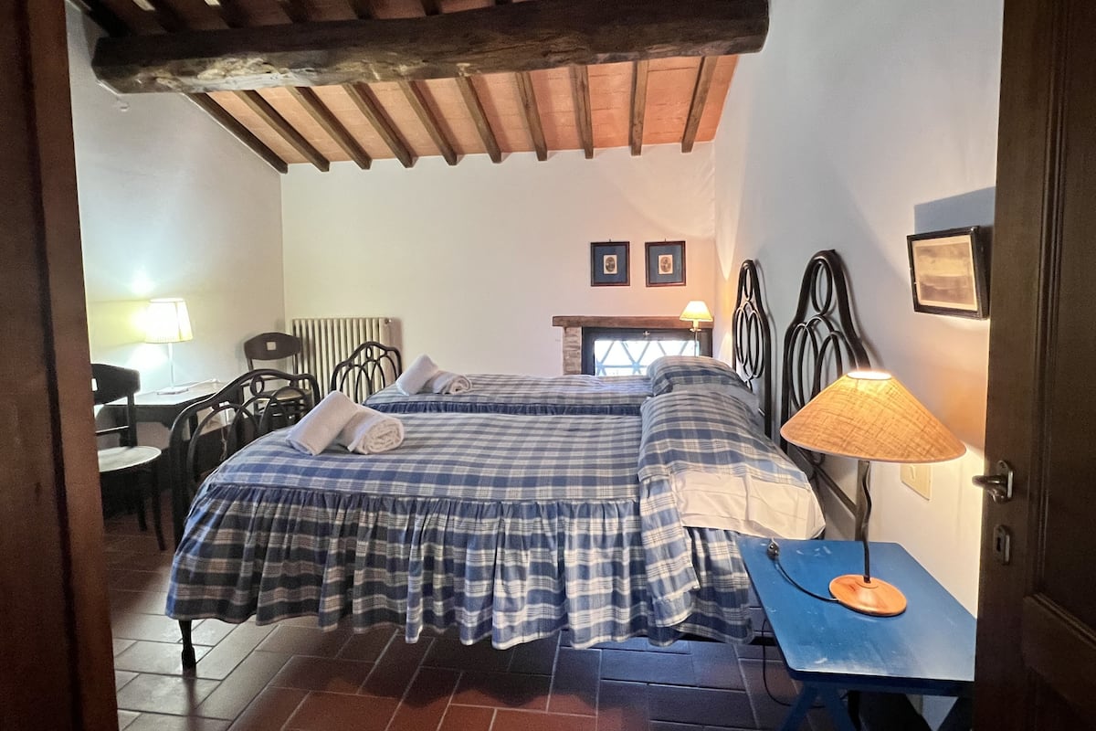 Een slaapkamer met een bed, een tafel met een lamp, een stoel, een open haard en een raam.