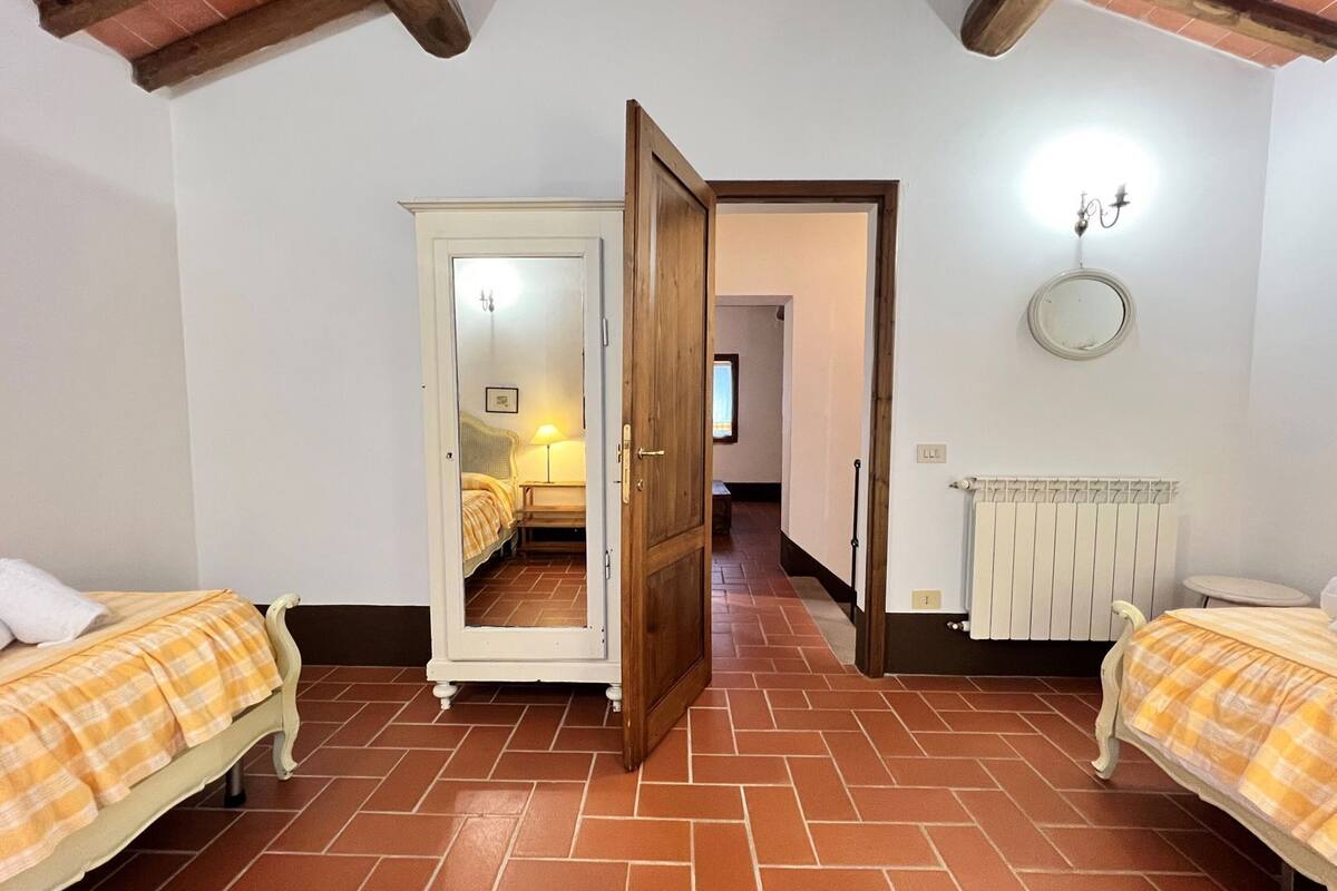 Een kamer met twee bedden, een radiator, een spiegel en een deur naar een andere kamer.
