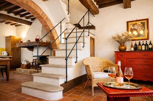 Un interior rústico con una escalera de piedra, muebles de mimbre y una exhibición de vinos.