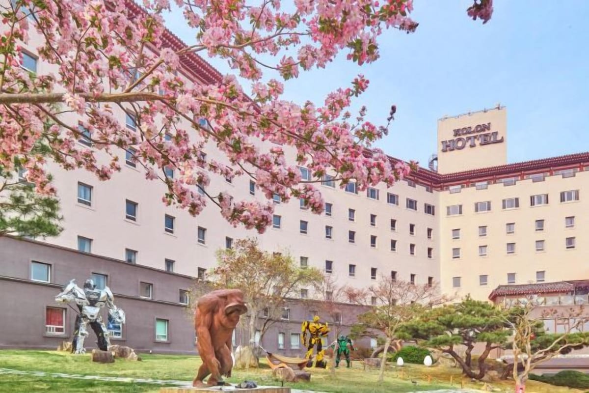 A hotel with a large building, a courtyard with sculptures, and cherry blossoms.