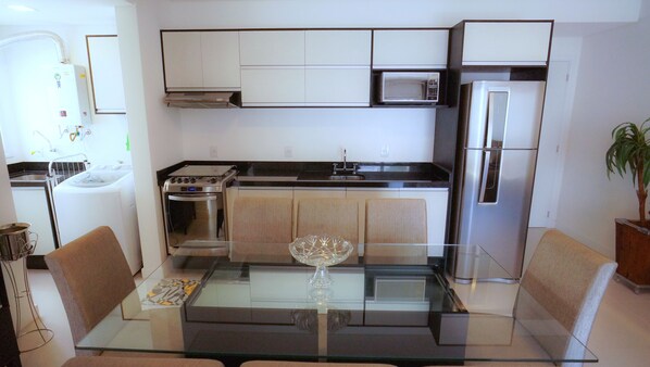 A compact kitchen with a glass-top table, stainless steel appliances, and a potted plant.