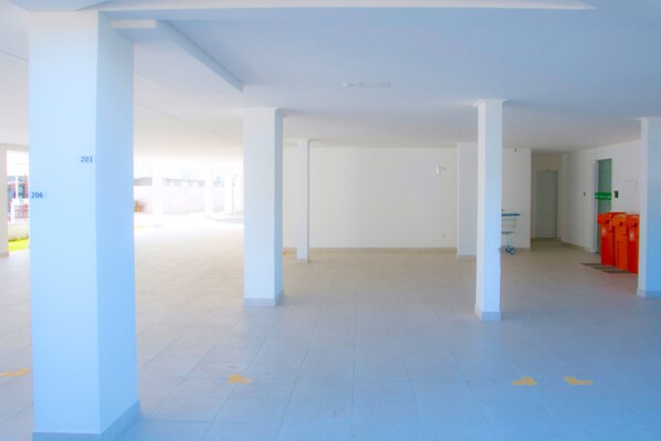 Amplio espacio interior, bien iluminado, con pilares blancos y suelo de baldosas, que presenta una puerta visible y un carrito de servicio al fondo.