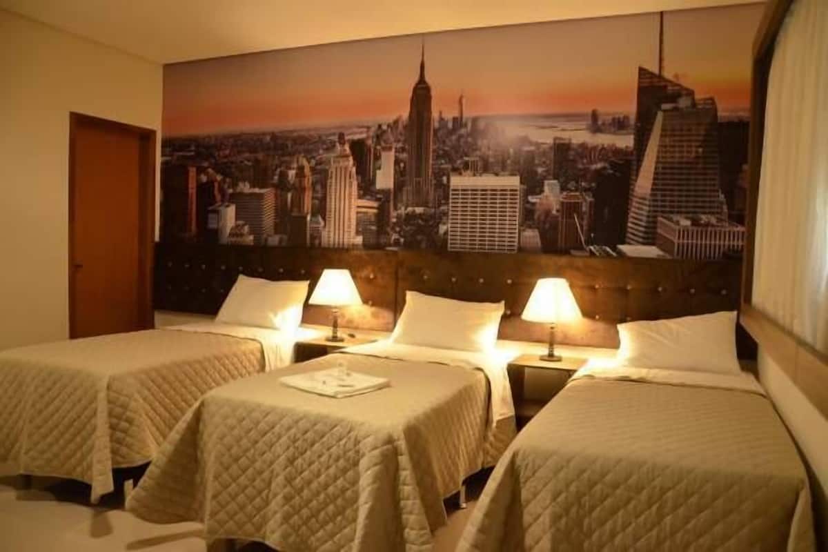 Ein Hotelzimmer mit zwei Betten, einer Stadtlandschaftsmalerei an der Wand und einer Tür links.